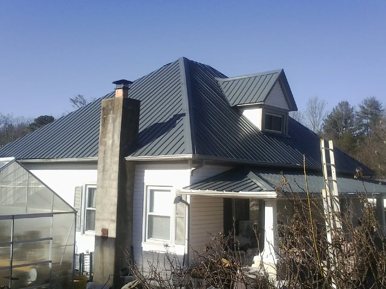Dark blue standing seam metal roof on a white farmhouse with dormer — Slate & Tile Roof Repair by Roofing Brothers in Meadow Grove