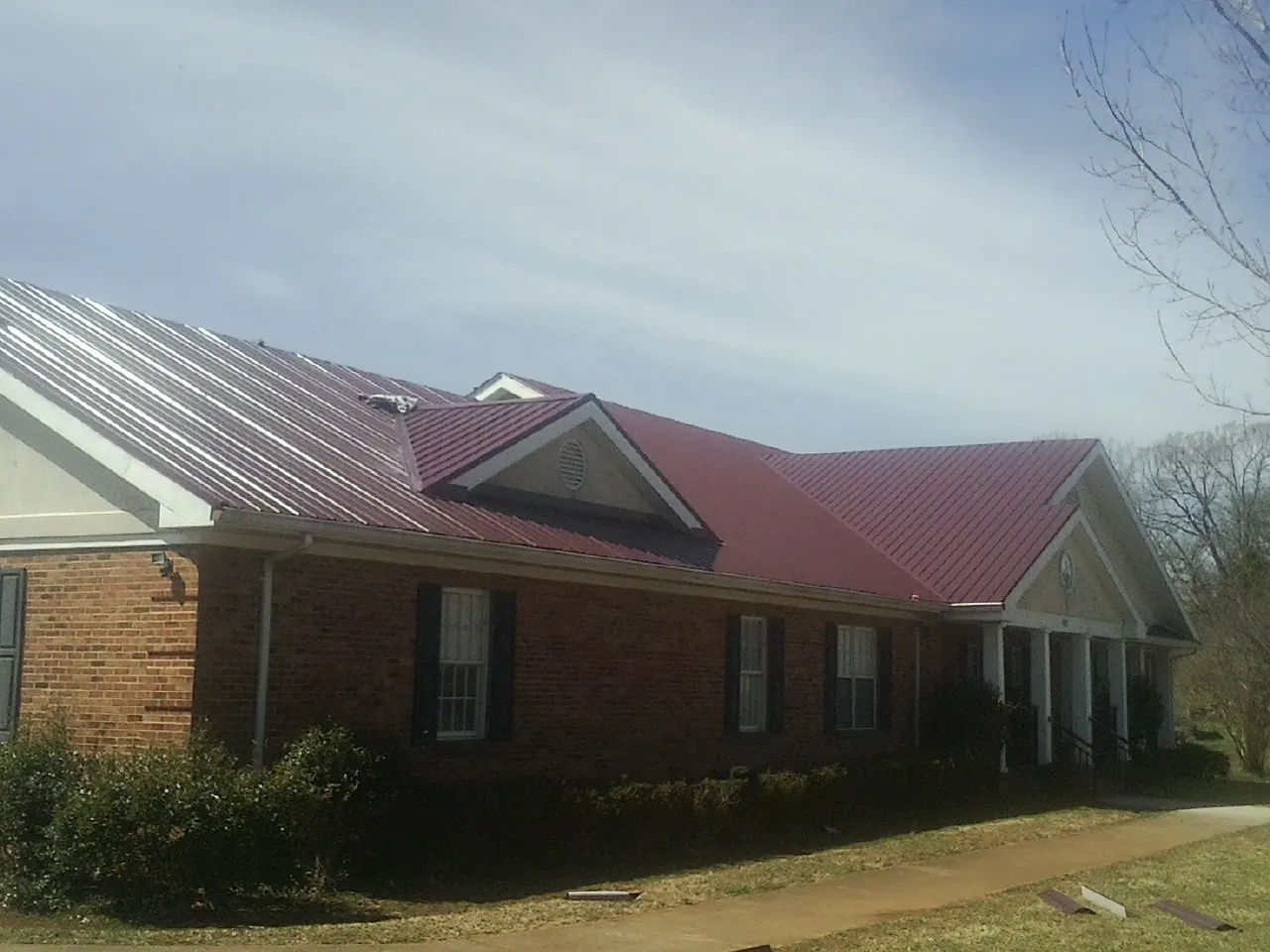 Red metal roof with gabled entries on a long brick building, from a Hail Damage Roof Repair job in Meadow Grove