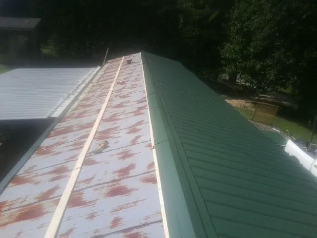 Old rusted panels beside newly installed green metal roofing — Wind Damage Roof Repair by Roofing Brothers in Meadow Grove