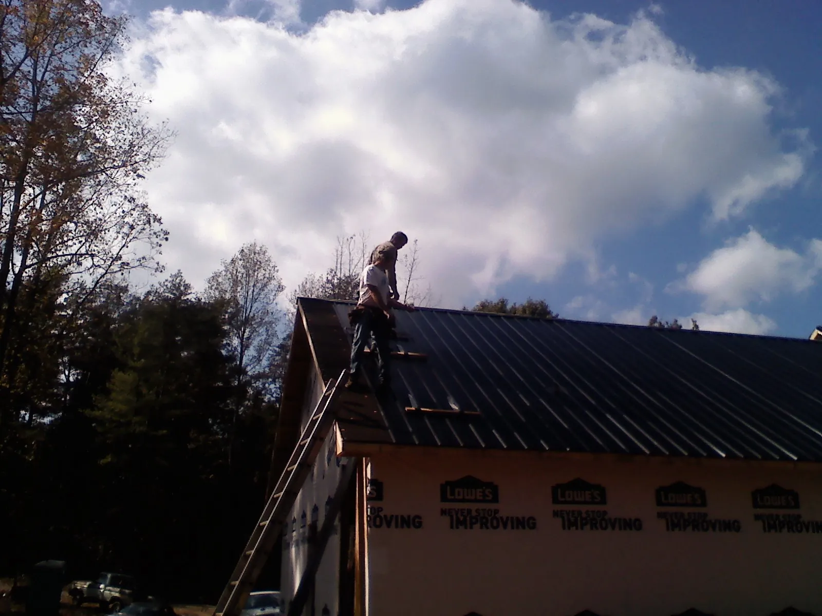 Roofer fastening dark metal panels high against a cloudy sky, from a Roof Inspection job in Meadow Grove