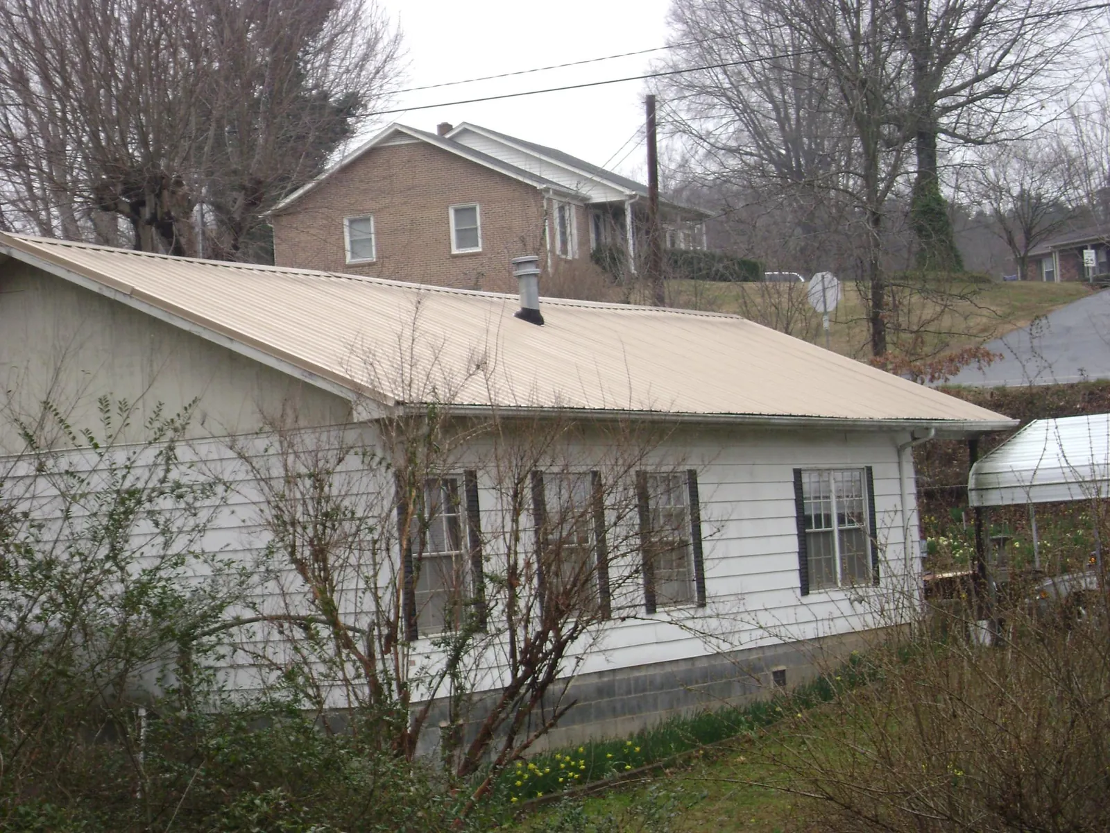 Tan metal roof on a white sided house set into a hillside — Commercial Roofing by Roofing Brothers in Meadow Grove