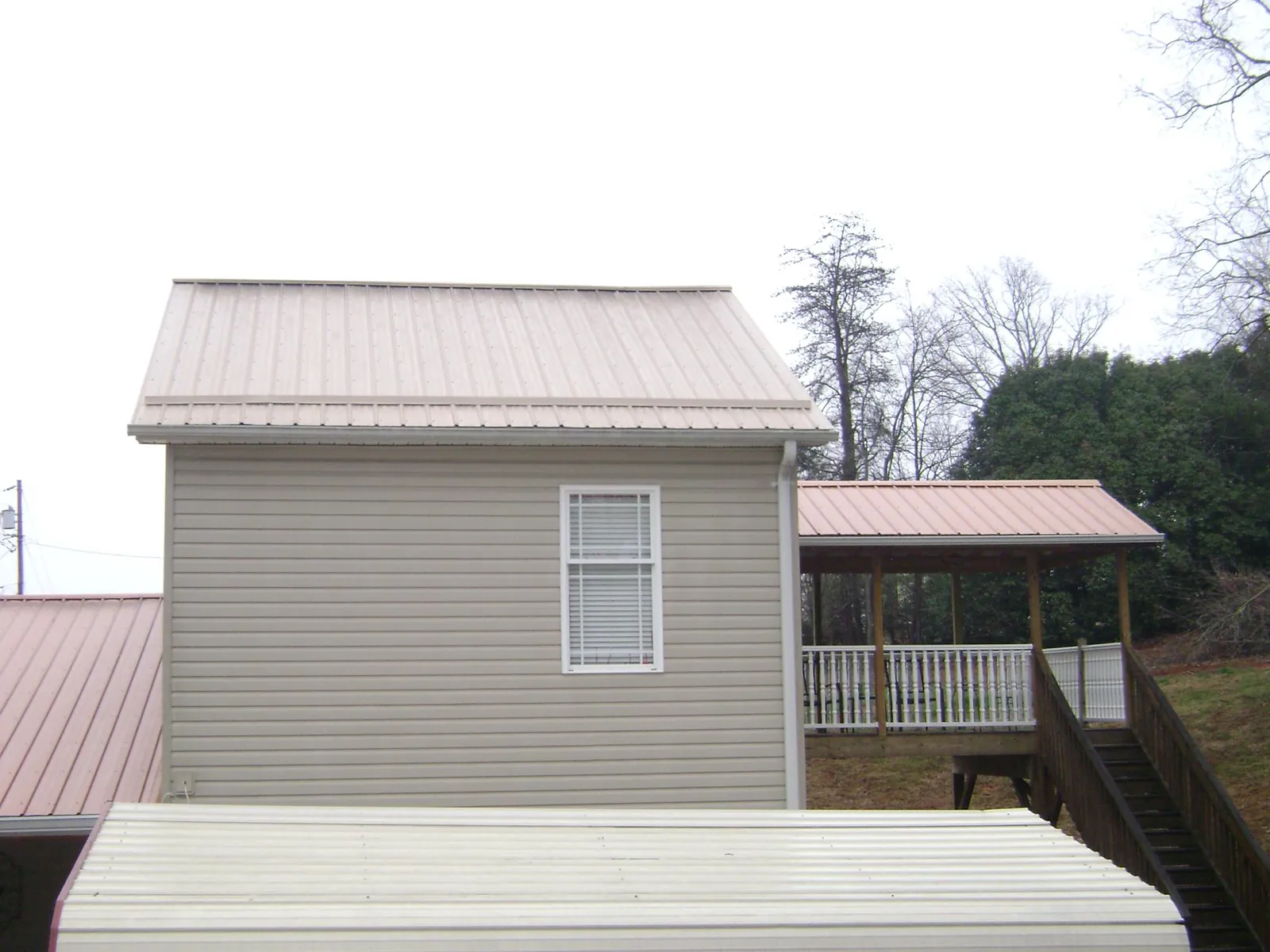 Tan metal roofs on a two story addition and attached porch, from a Roof Replacement job in Meadow Grove
